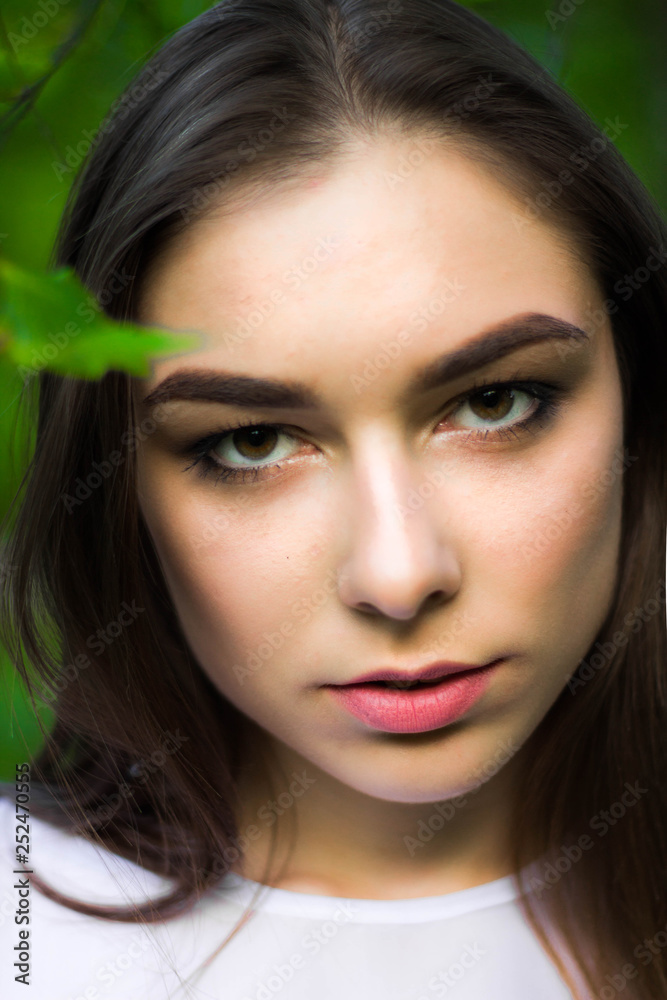 Portrait of a beautiful young woman on a background of green leaves, summer outdoors. Naturally beautiful woman smiling while standing among the green leaves.