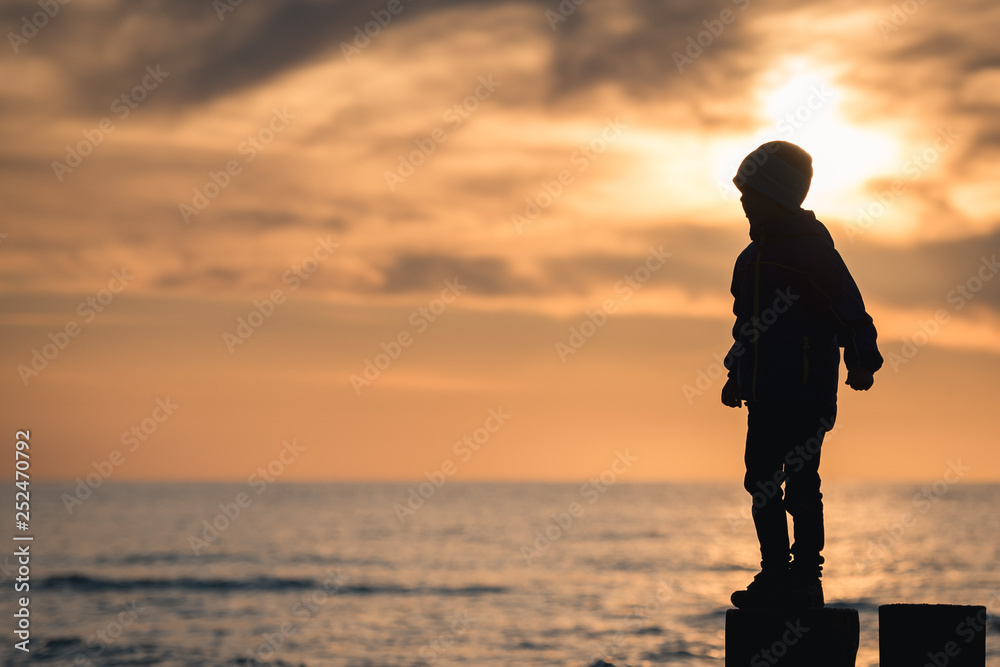 Silhouette of boy standing on breakwater stilt during sunset. Silhouette of boy standing on breakwater stilt during sunset.