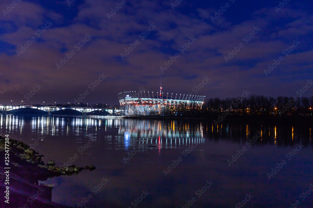 WARSAW, POLAND - FEBRUARY 14, 2019:Night illuminated skyline view with water reflections, National Stadium in Warsaw