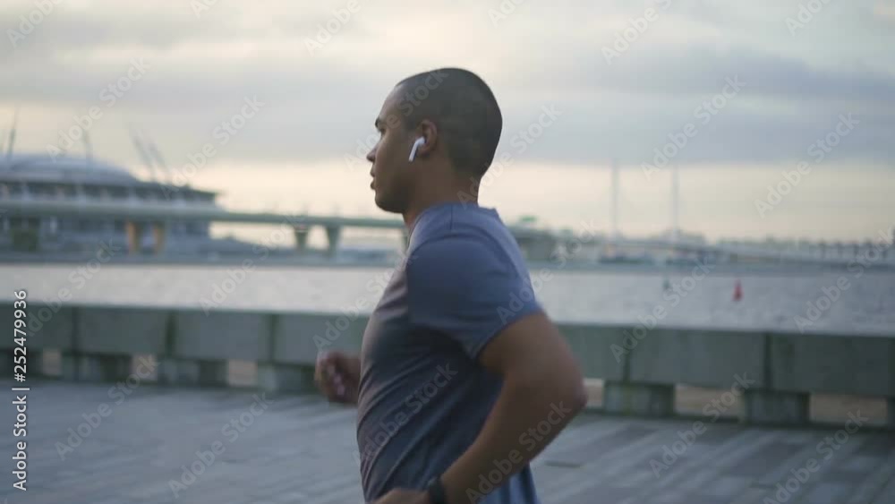 Face portrait of happy african american adult professional fashion man slow running and listening music in headphones. Black young afro american and active attractive male person training and jogging Face portrait of happy african american adult professional fashion man slow running and listening music in headphones. Black young afro american and active attractive male person training and jogging