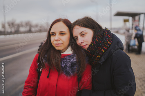 Two girls waiting for the bus at the bus station. Close up. The girls stand on the street