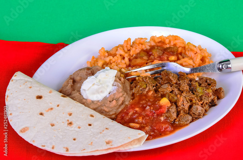 Carne Guisada dinner on white platter against red and green BG