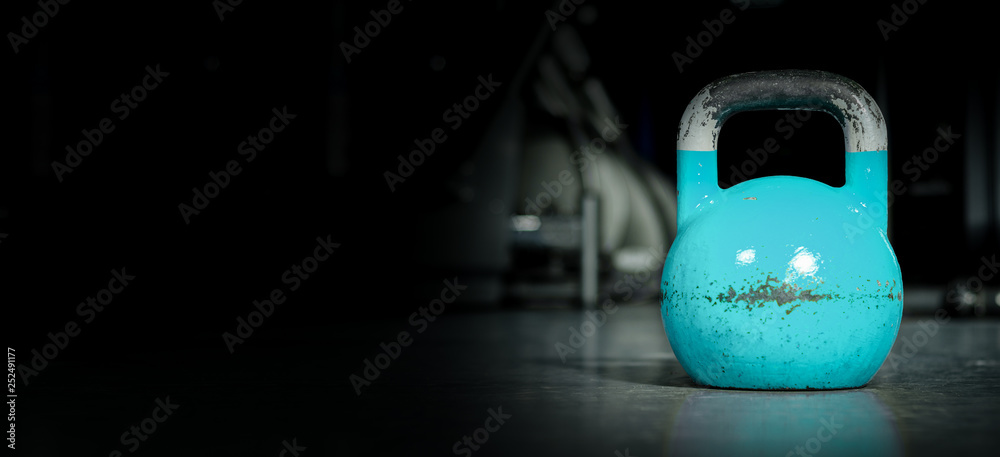 Heavy old used color kettlebell weight on the gym floor ready for fitness strength workout to build muscles with dark background and free copy space banner 