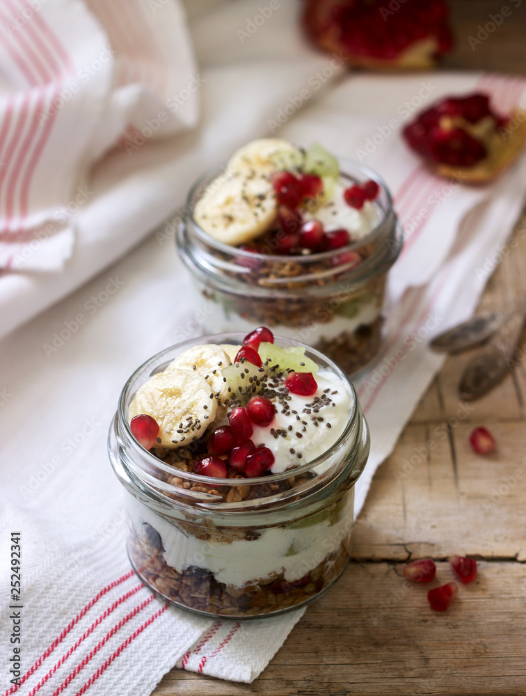 Granola with yogurt and fruit in glass jars on a wooden table. Rustic style. Granola with yogurt and fruit in glass jars on a wooden table. Rustic style.