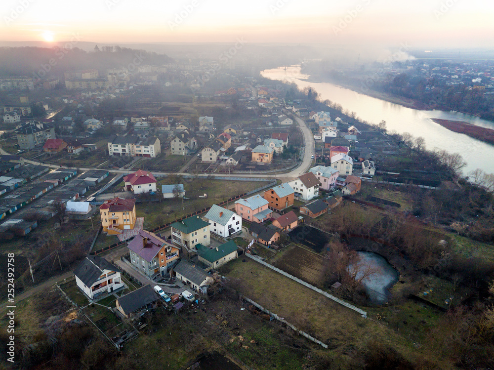 Naklejka premium Aerial top view of river flowing through town. Rural landscape of residential houses, roads and trees on spring or autumn day. Drone photography.