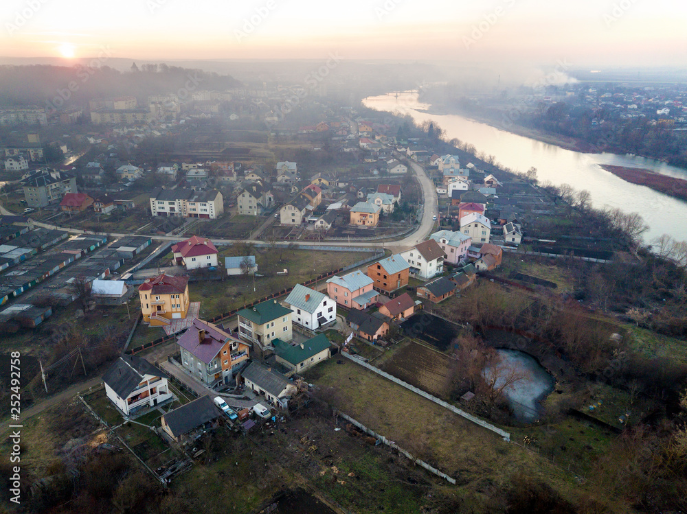 Aerial top view of river flowing through town. Rural landscape of residential houses, roads and trees on spring or autumn day. Drone photography.