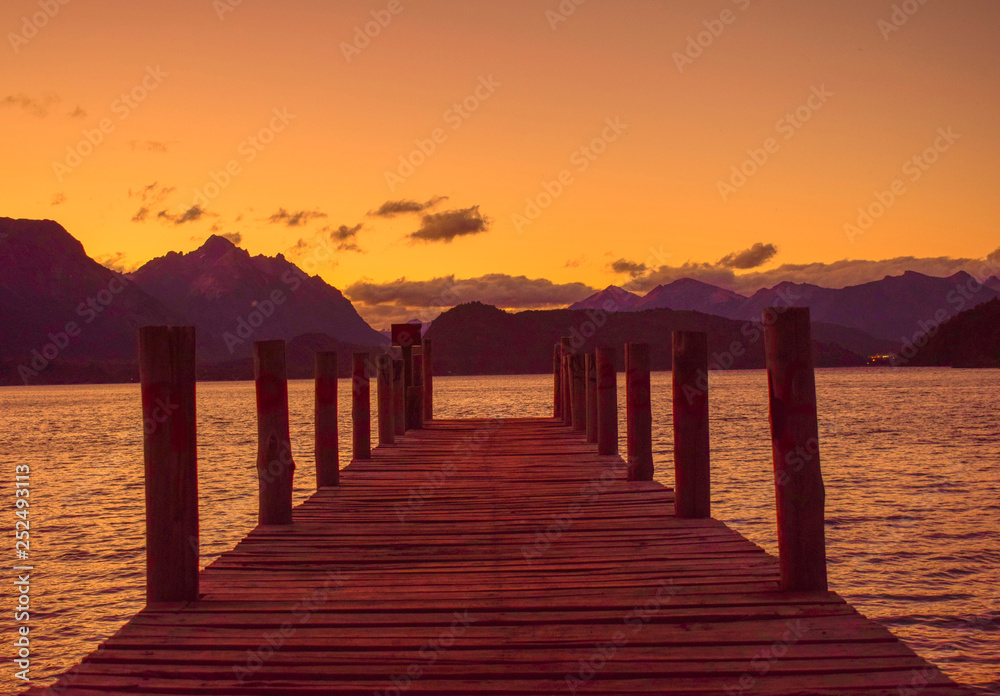 viejo muelle sobre un lago  rodeado de montañas sobre el cual se reflejan los ultimos rayos de sol