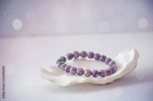 Tela An amethyst bracelet in a seashell with a white and purple bokeh background