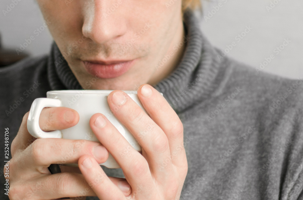 young man in a gray sweater with a Cup of coffee in his hands young man in a gray sweater with a Cup of coffee in his hands