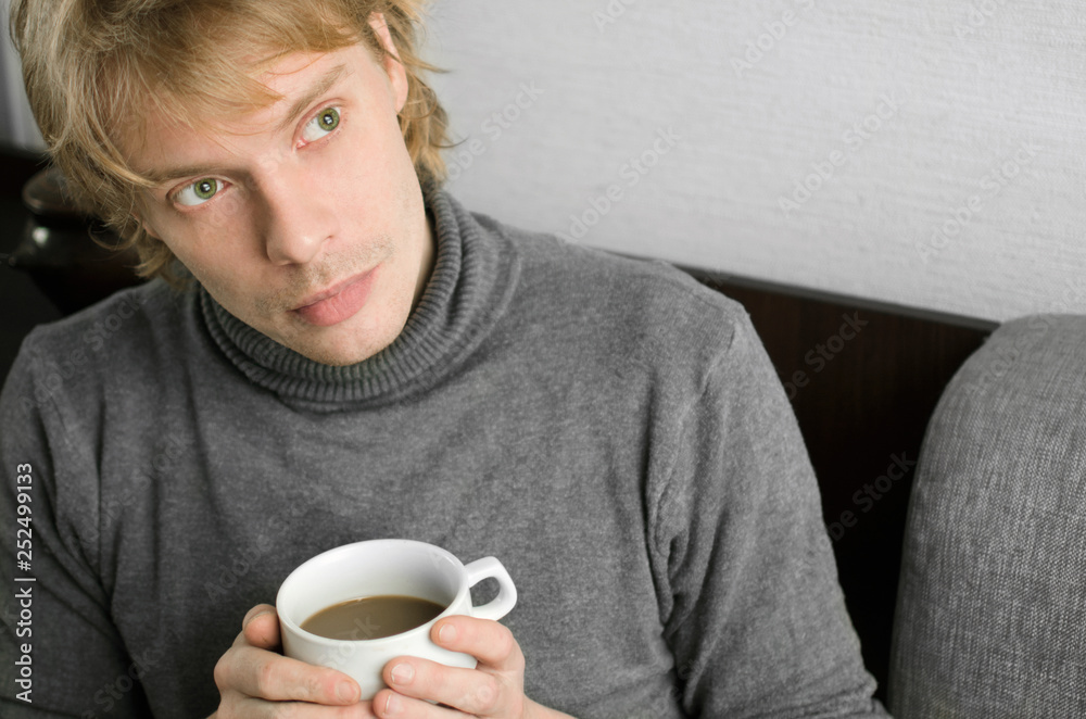 young man in a gray sweater with a Cup of coffee in his hands young man in a gray sweater with a Cup of coffee in his hands