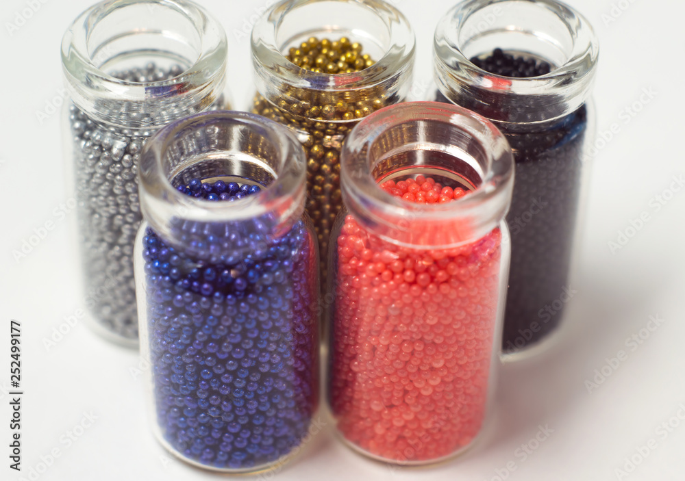 Multicolored beads in glass jars. Beads are poured on a white background. Plastic multi-colored polymers. Plastic pillets. Multicolored beads in glass jars. Beads are poured on a white background. Plastic multi-colored polymers. Plastic pillets.