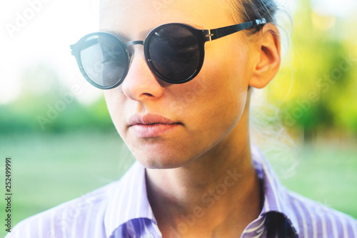 Portrait of a Young Woman in Sunglasses on a Background of Green Foliage at Sunset Time. Sunny Summer Weather