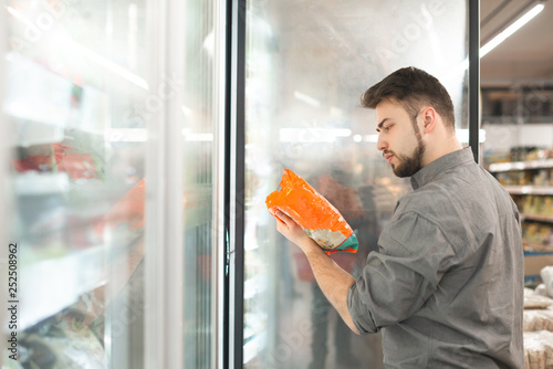 Cuadro en lienzo Buyer standing in the supermarket near the refrigerator holds the package in his hand and reads the label