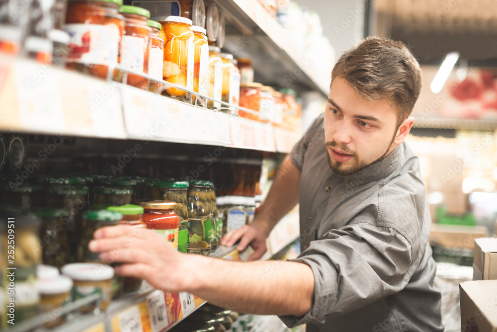 Man takes a can of vegetables with a shelf from a grocery store.Choosing and buying canned tomatoes in a supermarket. Man buys products in a supermarket, takes from a shelf. Man buys canned vegetables
