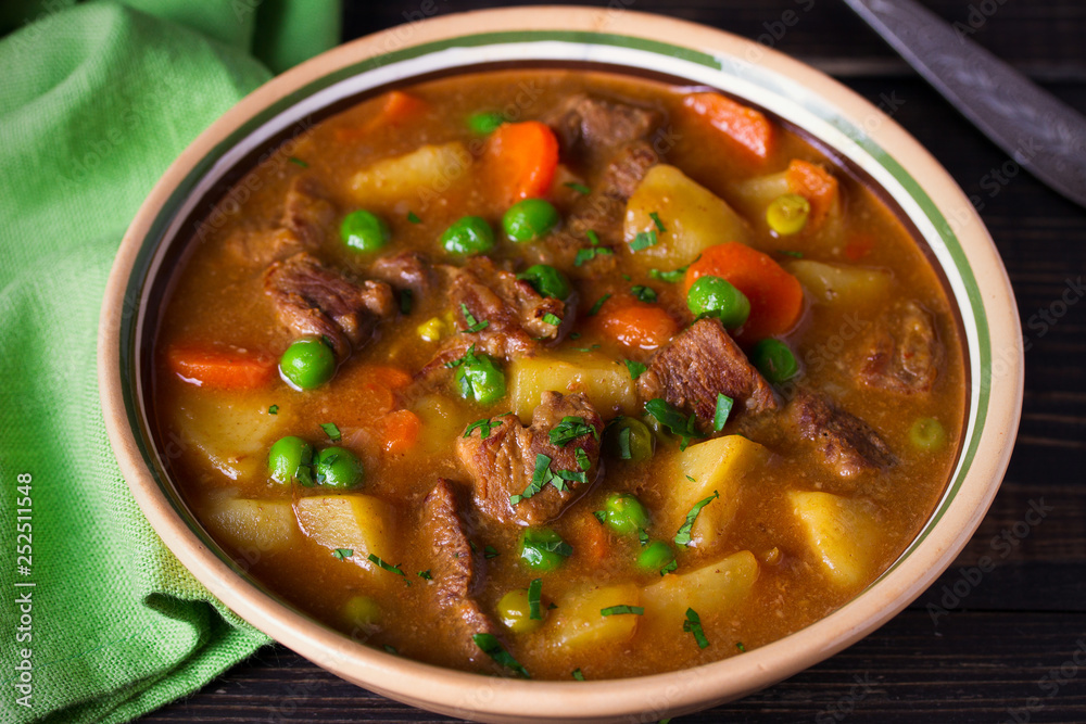 Homemade Irish beef stew with potatoes, carrots and peas in bowl on wooden table. horizontal Homemade Irish beef stew with potatoes, carrots and peas in bowl on wooden table. horizontal
