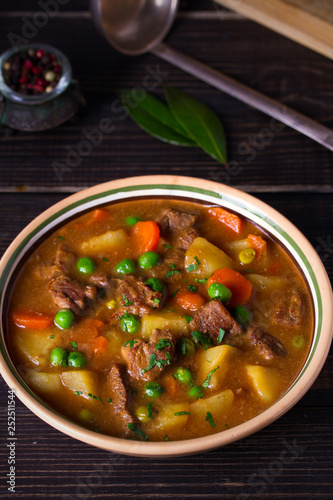 Homemade Irish beef stew with potatoes, carrots and peas in bowl on wooden table. vertical