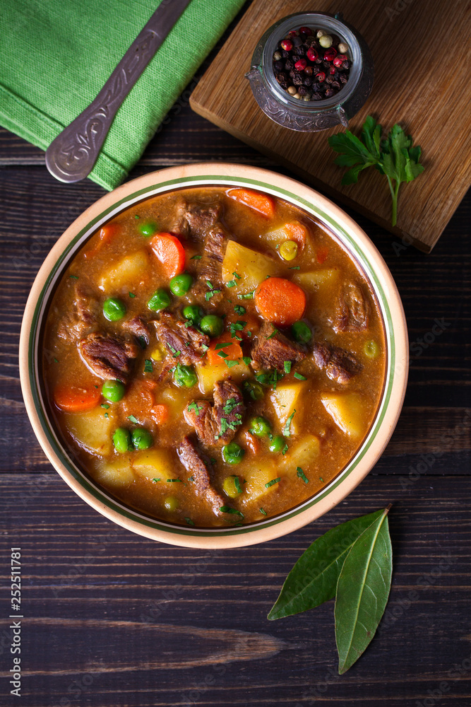 Homemade Irish beef stew with potatoes, carrots and peas in bowl on wooden table. overhead, vertical Homemade Irish beef stew with potatoes, carrots and peas in bowl on wooden table. overhead, vertical