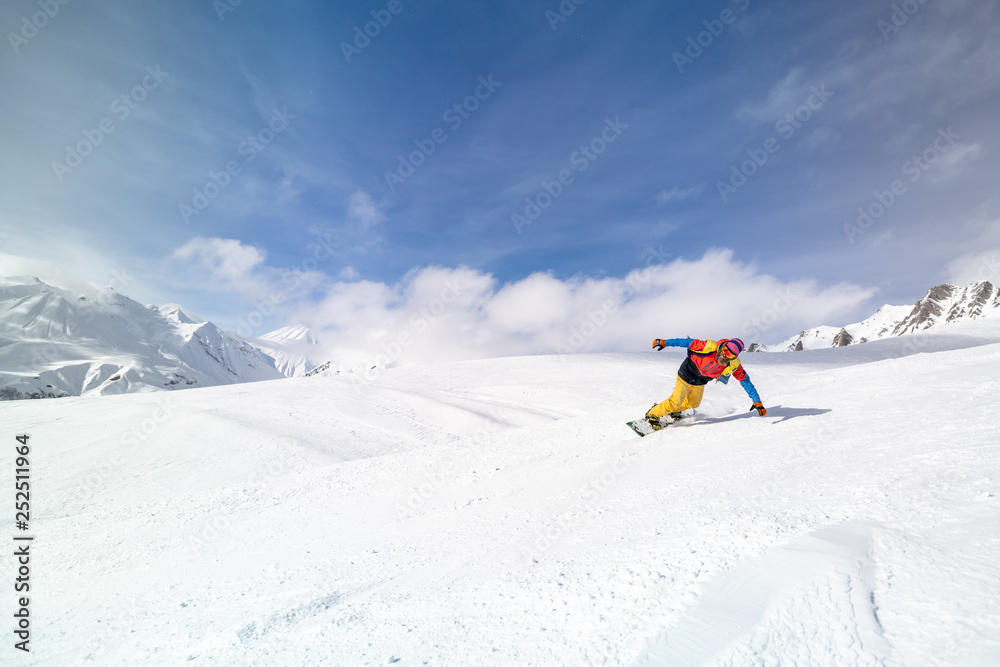 Active man snowboarder riding on slope during beautiful sunny day in the ountains.