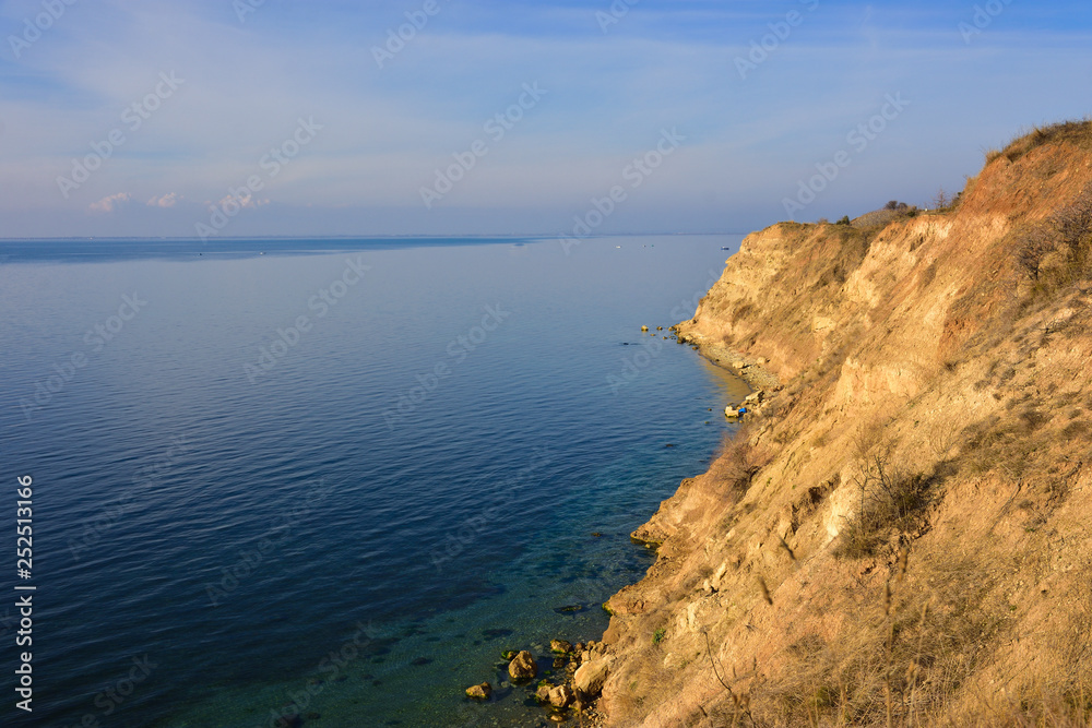 High gravel cliff by blue Greek sea on sunny day