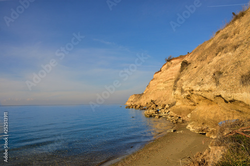 High gravel cliff by blue Greek sea on sunny day