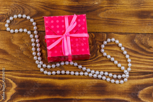 Gift box and pearl necklace on wooden background