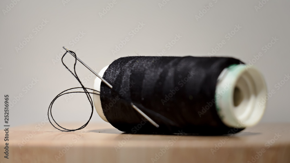 Rollo de hilo de coser negro, con aguja atravesándolo. Fondo blanco y luz directa sobre el objeto. Hilo de coser. Rollo de hilo de coser negro, con aguja atravesándolo. Fondo blanco y luz directa sobre el objeto. Hilo de coser.