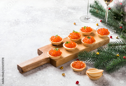Christmas and New Year holidays composition. Red Salmon Caviar in wooden bowl, Tartlets Festive Appetizer and champagne on  gray background.Copy space for Text.