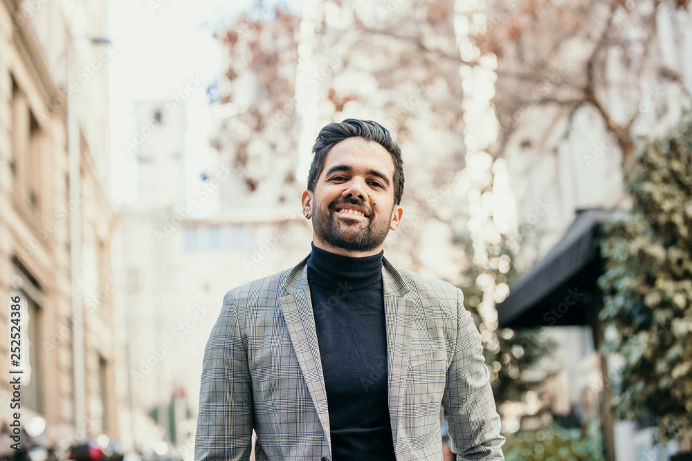 Portrait of smiling latin bearded man walking in the city centre.