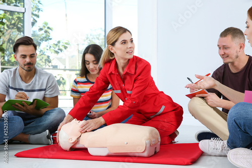 Instructor demonstrating CPR on mannequin at first aid class indoors