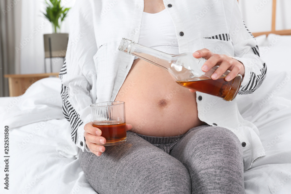 Pregnant woman pouring whiskey into glass at home. Alcohol addiction Pregnant woman pouring whiskey into glass at home. Alcohol addiction