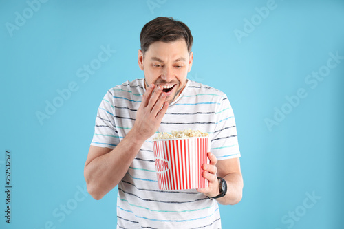 Emotional man with tasty popcorn on color background