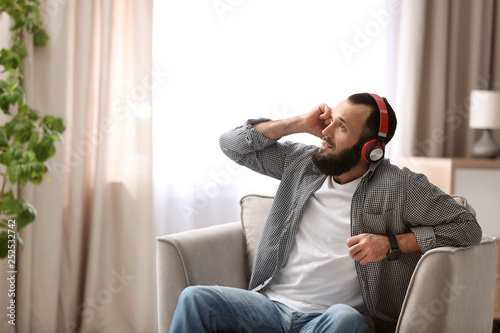 Mature man with headphones resting in armchair at home © New Africa