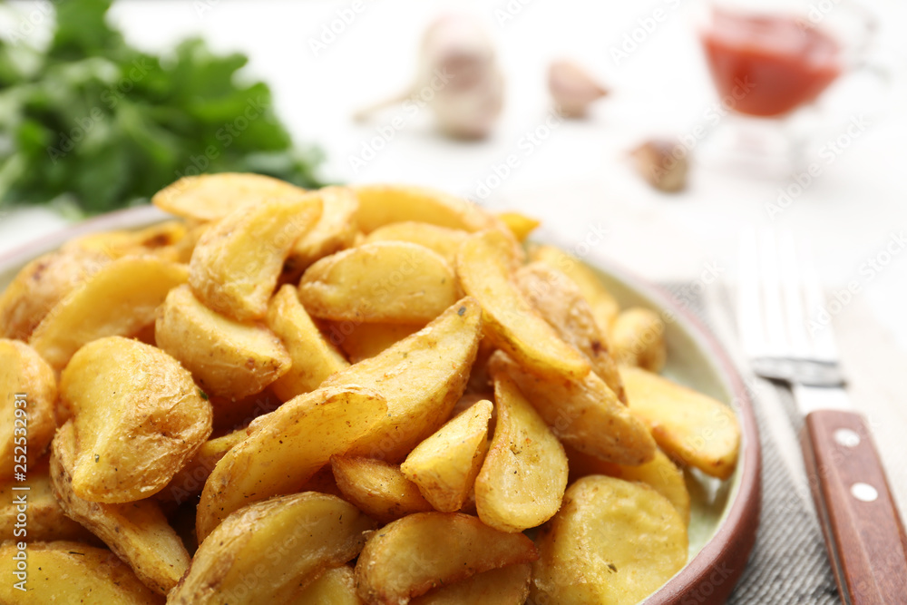 Plate with tasty baked potato wedges on table, closeup
