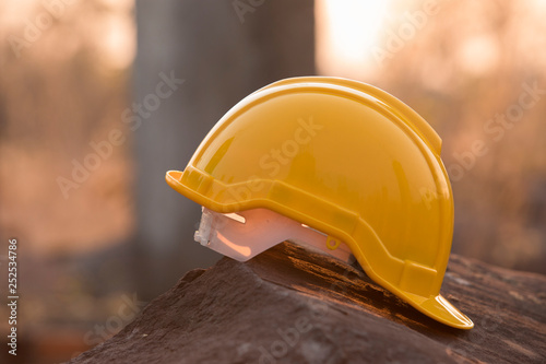 Fototapeta Naklejka Na Ścianę i Meble -  Helmet in the construction site, Yellow helmet on stone, background, steel structure and sunset
