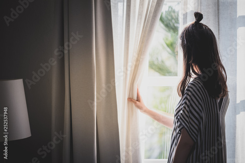 woman opening curtain looking through window
