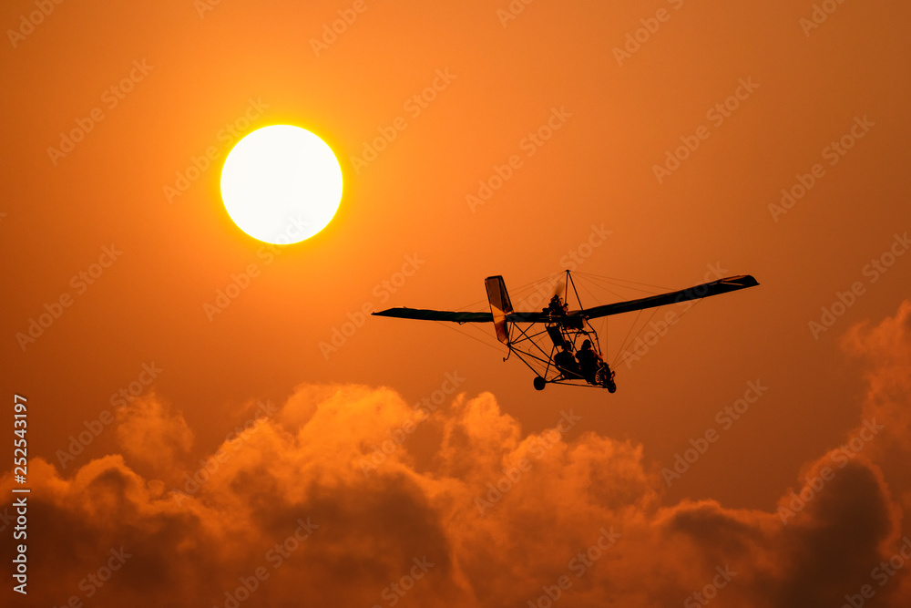 A microlight aircraft with two passengers with the sun and cloud A microlight aircraft with two passengers with the sun and cloud