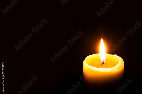 Single Burning Yellow Candle Glowing on a Dark Background. Copy Space.
