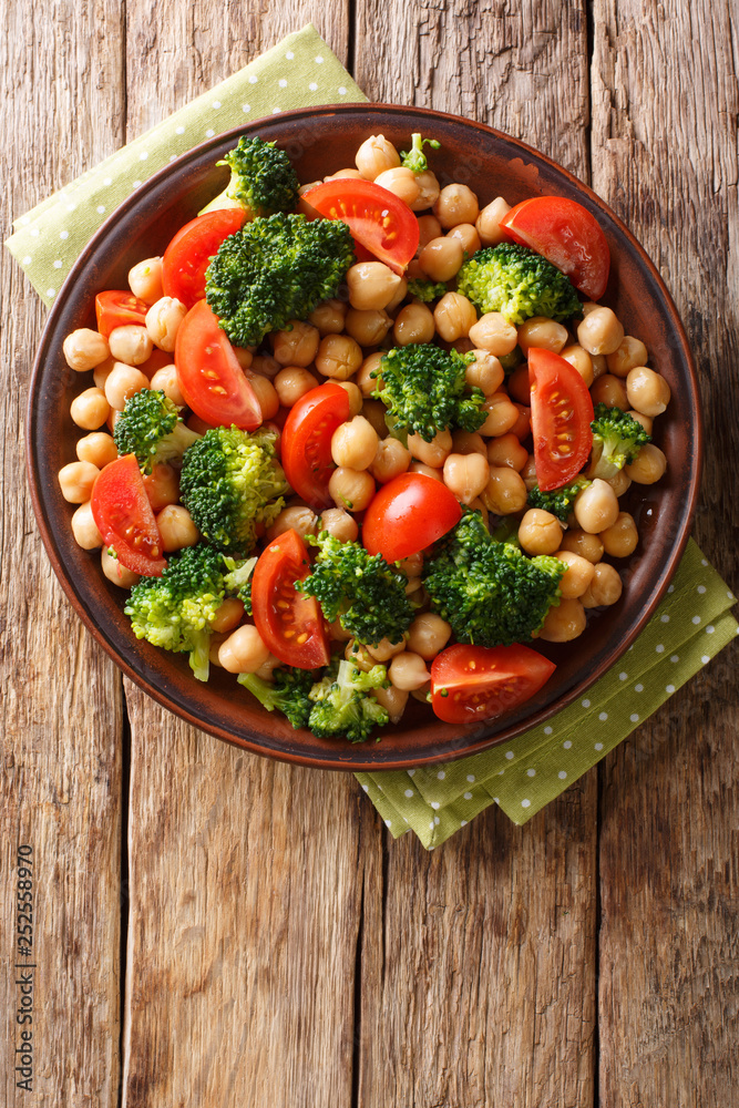 Delicious salad of broccoli, chickpeas and tomatoes closeup on a plate. Vertical top view