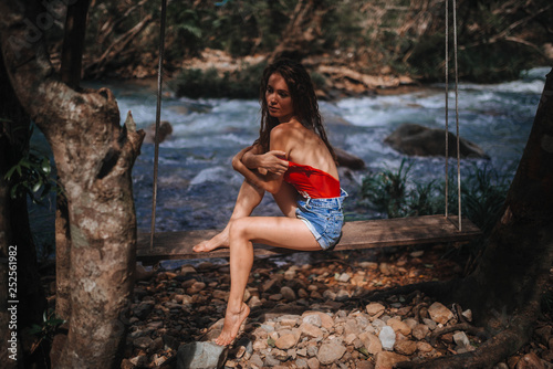  girl in a red swimsuit on a stump in the jungle near the waterfall