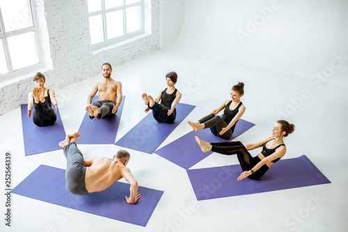 Group of young people practising yoga with experienced senior trainer in the white spacious studio