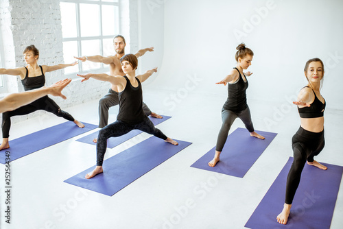 Group of young people practising yoga with experienced senior trainer in the white spacious studio