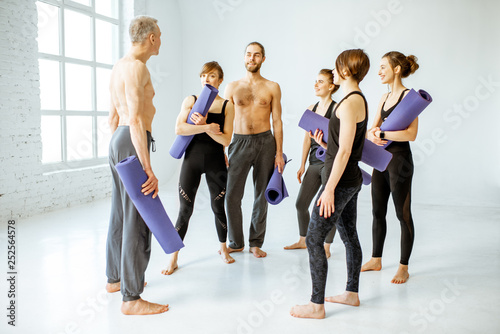 Group of young people standing together and talking with senior instructor during the break after the yoga training in the white studio