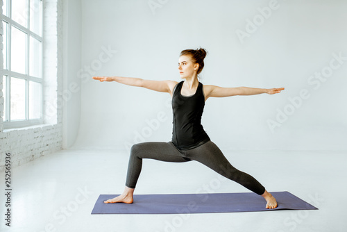Young woman keeping pose, practising yoga in the white studio