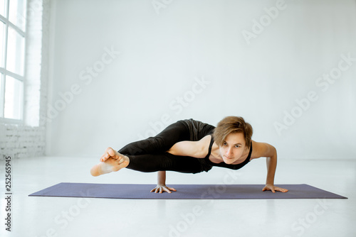 Young woman keeping pose, practising yoga in the white studio