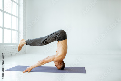 Senior athletic man with naked torso practising yoga poses in the white studio