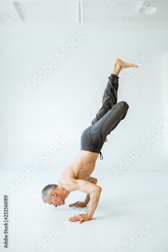 Senior athletic man with naked torso practising yoga poses in the white studio