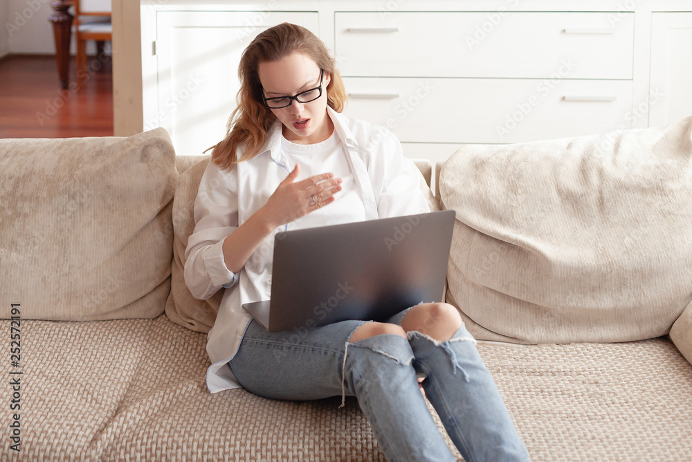 Fototapeta premium Happy young business woman in casual wear talking on video using a laptop with her colleagues on the sofa in the living room of her home