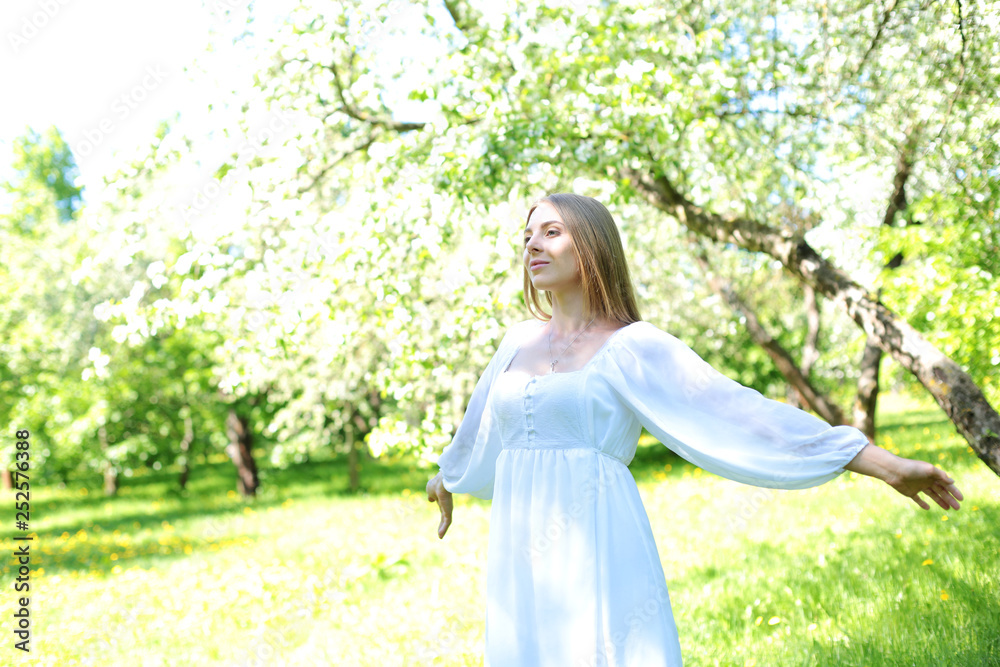 Happy blonde woman on a background of blooming spring garden with her hands raised to the sky Happy blonde woman on a background of blooming spring garden with her hands raised to the sky
