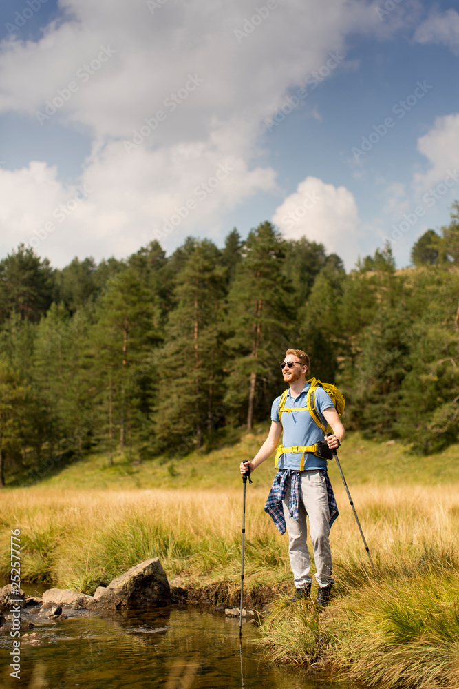 Young man crosses a mountain stream on a sunny day