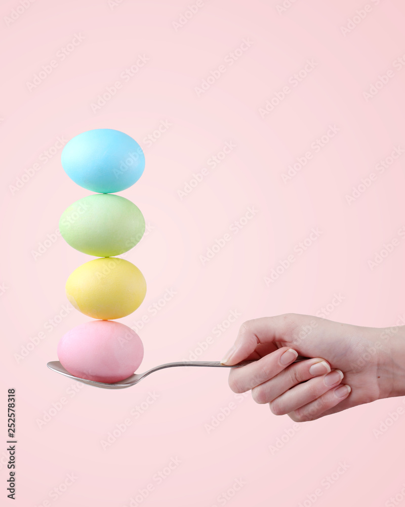 Female hand holds a spoon on which multi-colored eggs are balanced, on a pink background. Unusual design, Easter concept, copy space. Female hand holds a spoon on which multi-colored eggs are balanced, on a pink background. Unusual design, Easter concept, copy space.